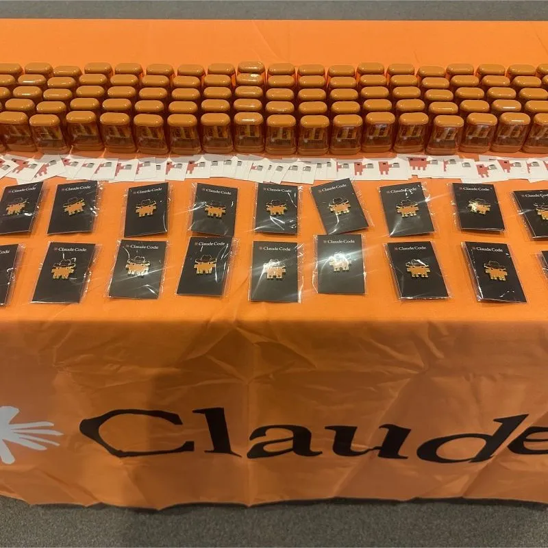 A Claude-branded table laid out with Claude Code pins, stickers, and swag before an event