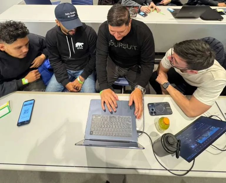 Four people huddled around a laptop, watching a build run at a Claude developer session